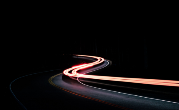 Time-lapse of a car passing at night, creating a stream of light down a winding road